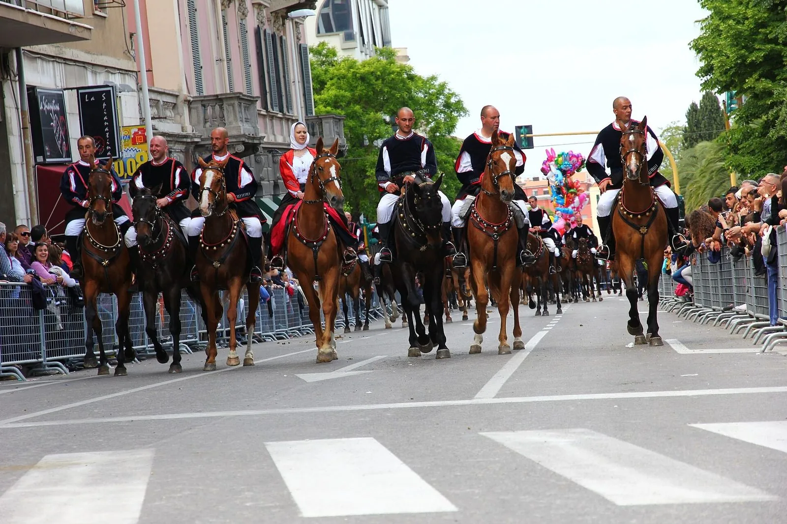 Cavalieri in costume tradizionale sardo sfilano a cavallo lungo un viale di Sassari tra due ali di pubblico