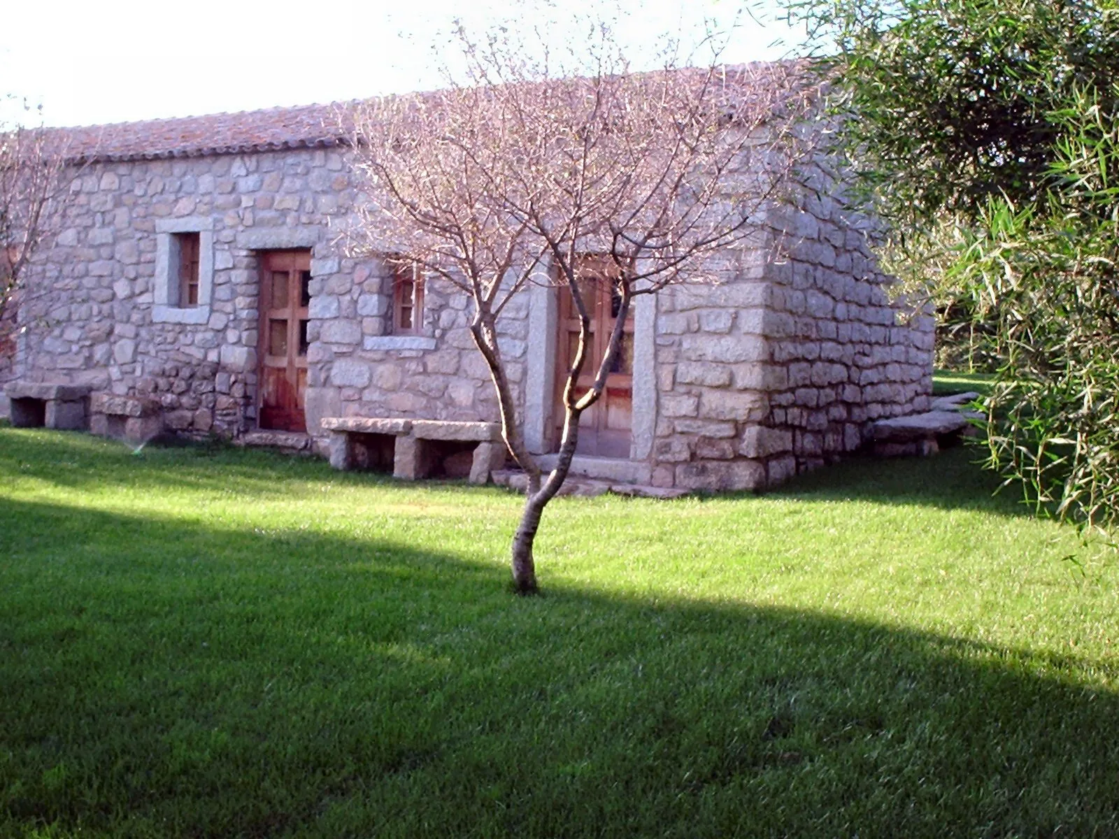 Uno stazzo gallurese restaurato: casa rurale bassa in blocchi di granito, con tetto di coppi e panche di pietra sul prato